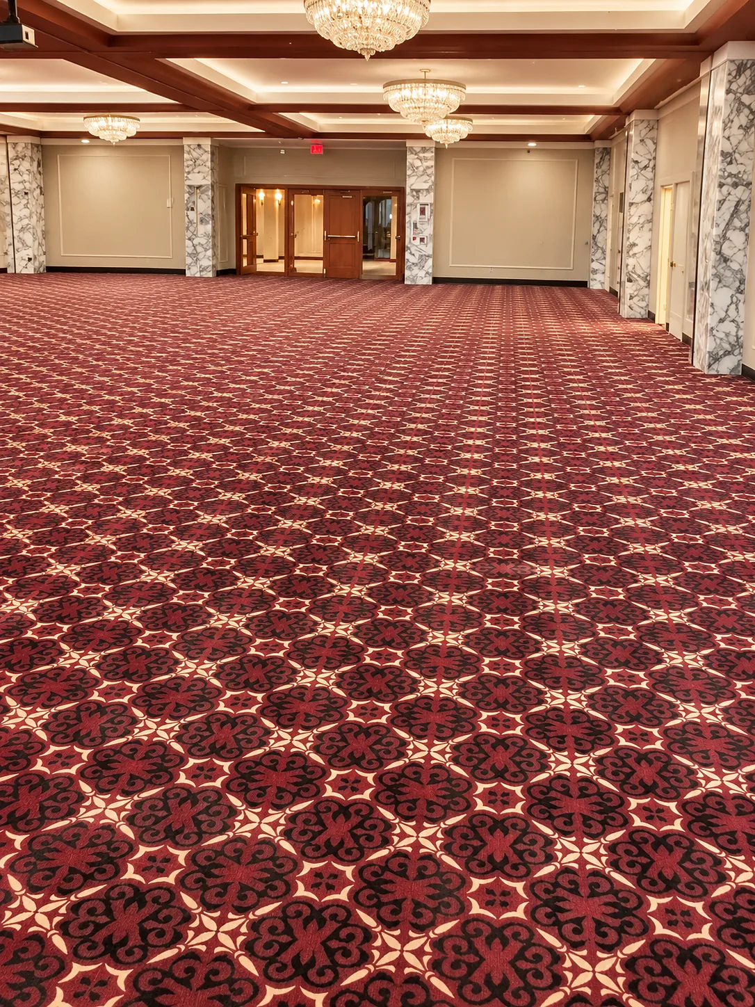 Large commercial ballroom with marble columns, chandeliers and an intricate red, black and cream patterned carpet